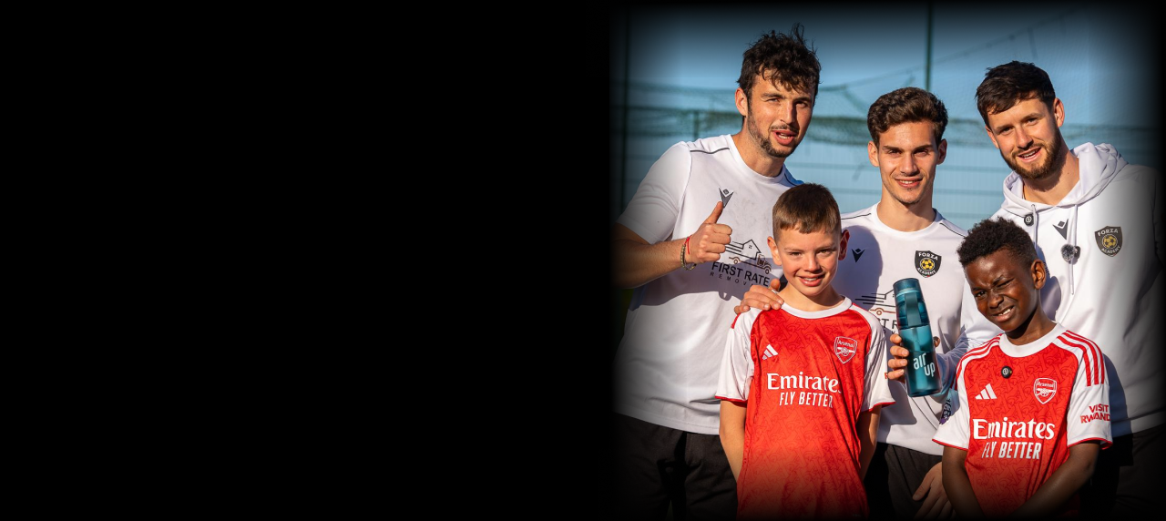 Coach and player training on a floodlit football pitch at dusk